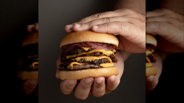 Person holding a cheeseburger with four patties plus toppings.