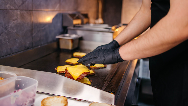 Chef cooking cheese burgers in a restaurant kitchen.