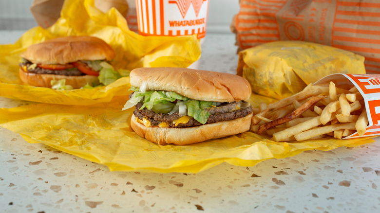 Burgers, fries, and a beverage from Whataburger spread out on table.