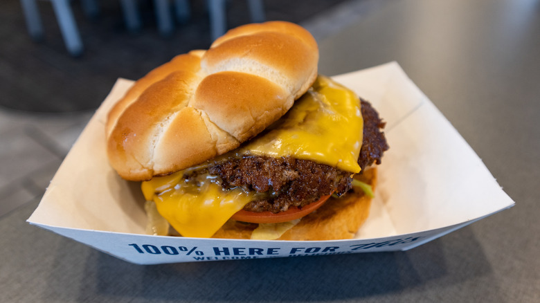 Culver's ButterBurger with cheese and tomato on paper tray inside restaurant.