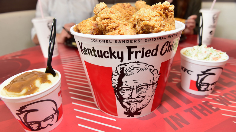 A bucket of KFC chicken with mashed potatoes, gravy, and coleslaw on the side.
