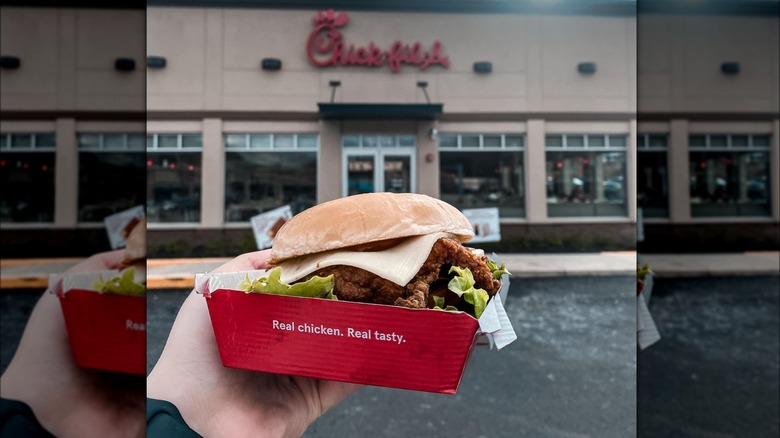 Person holding box with the Spicy Deluxe Chick-fil-A sandwich outside of the restaurant.
