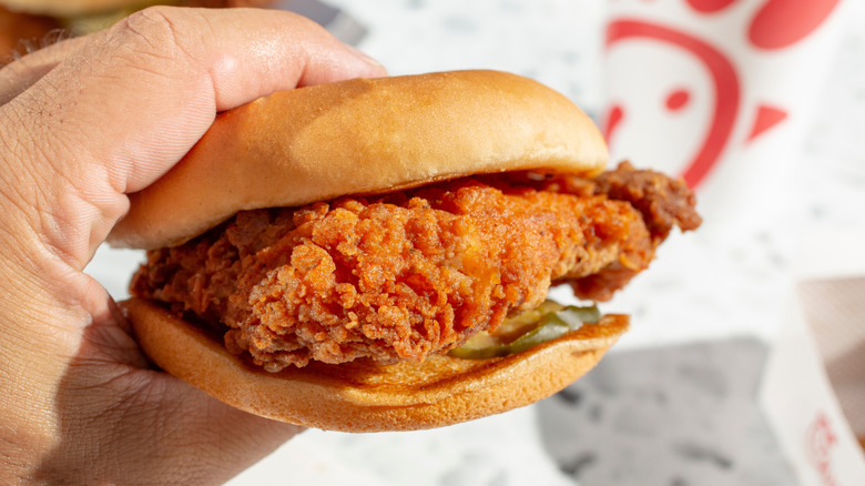 Person holding a classic Chick-fil-A sandwich with a beverage in the background.