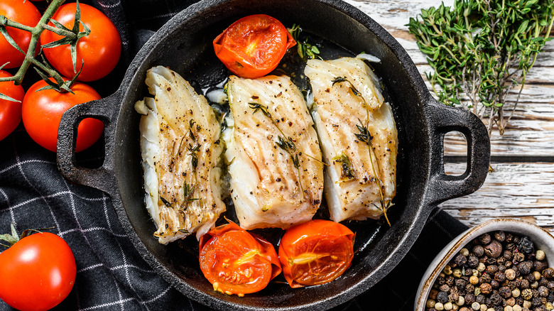 Three pieces of fish in iron skillet with tomatoes