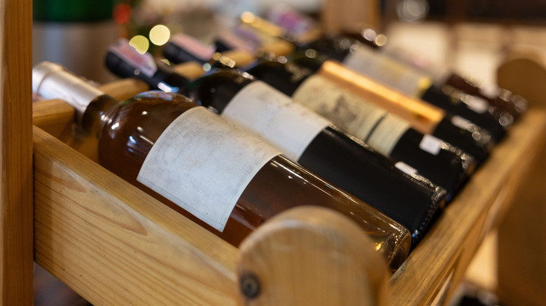 Row of various bottled wines on wooden rack.