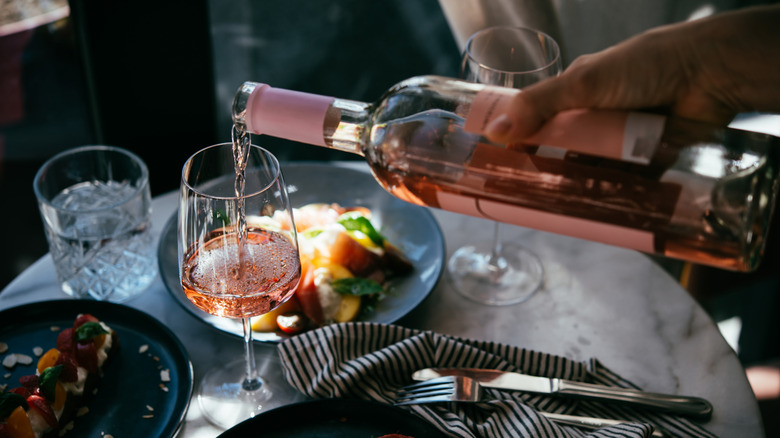 Hand pouring rosé wine into glass on table with meal.