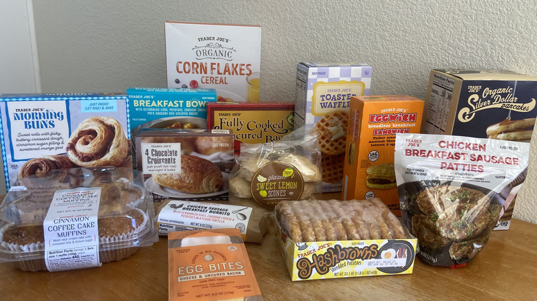 diagonal angle of many Trader Joe's breakfast foods in packaging on table, including corn flakes, morning buns, and eggwich sandwich