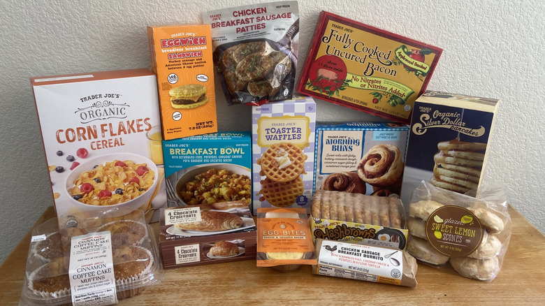 Several Trader Joe's breakfast foods in packaging stacked on table, including organic silver dollar pancakes, toaster waffles, and fully cooked uncured bacon