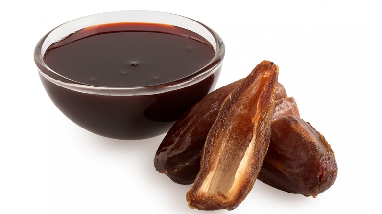 glass bowl of date syrup next to dried dates