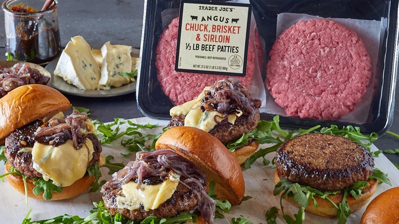 Package of beef patties behind three gourmet burgers with lots of toppings.