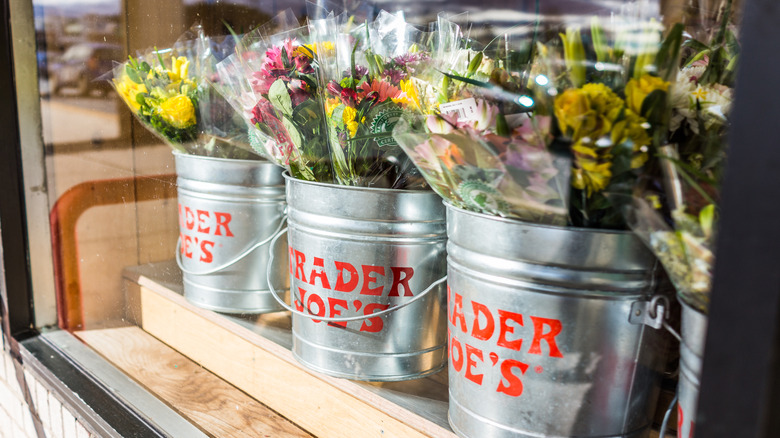 Metal buckets with Trader Joe's brand on front holding plastic-wrapped bouquets of flowers.