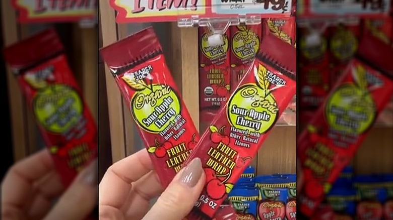 Hand holding two individually wrapped strips of fruit leather in sour apple cherry flavor.