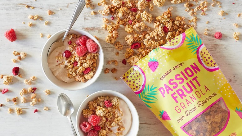 Open bag of passion fruit flavored granola with dried raspberries next to two bowls with spoons.