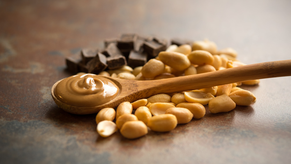 Chocolate and peanuts under wooden spoon with peanut butter