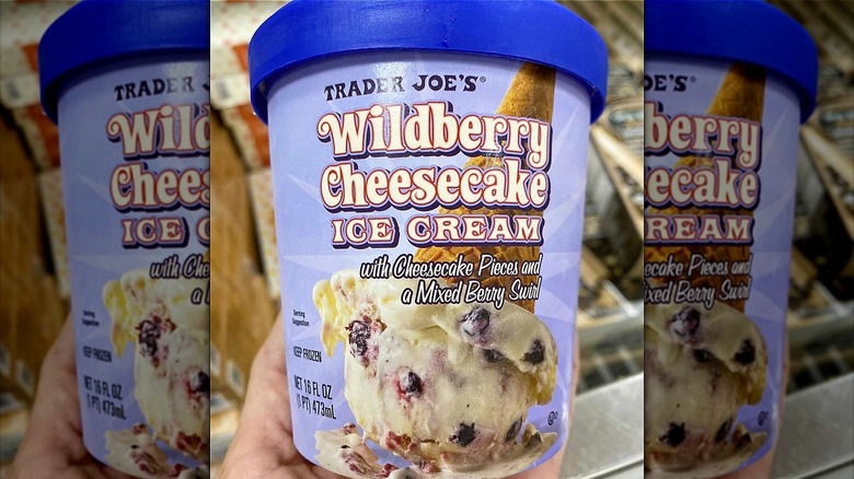 person holding Trader Joe's wildberry cheesecake ice cream in freezer aisle of store