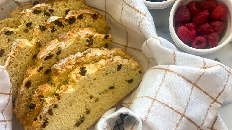 slices of traditional Irish soda bread in a towel-lined basket near a white bowl of ripe red raspberries