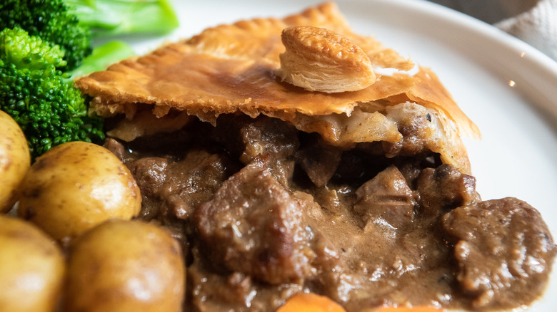 Slice of steak and kidney pie on plate with broccoli and potatoes