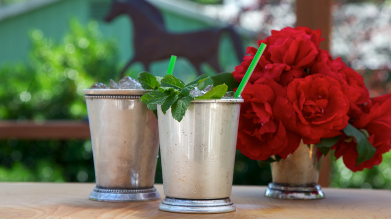 MInt-garnished drinks in silver cups in front of horse statue with roses