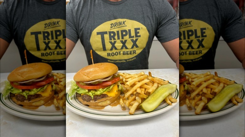 Person wearing XXX shirt behind burger and fries on white plate