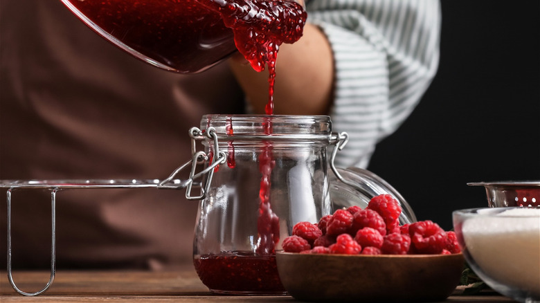 woman pouring raspberry jam into a jar