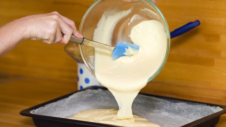 person pouring bowl of yellow cake batter into baking pan