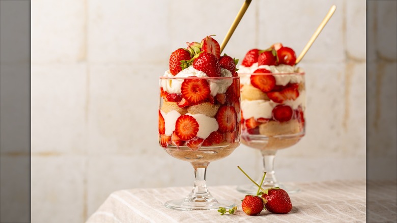 two strawberry trifle desserts in cups with straws