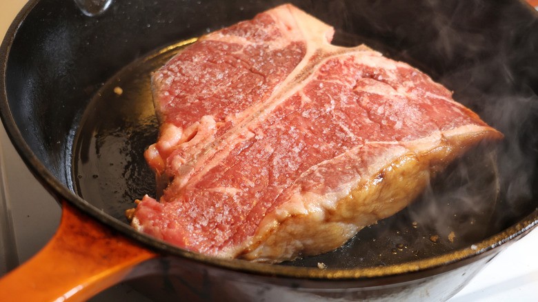 salted t-bone steak in smoking cast iron skillet