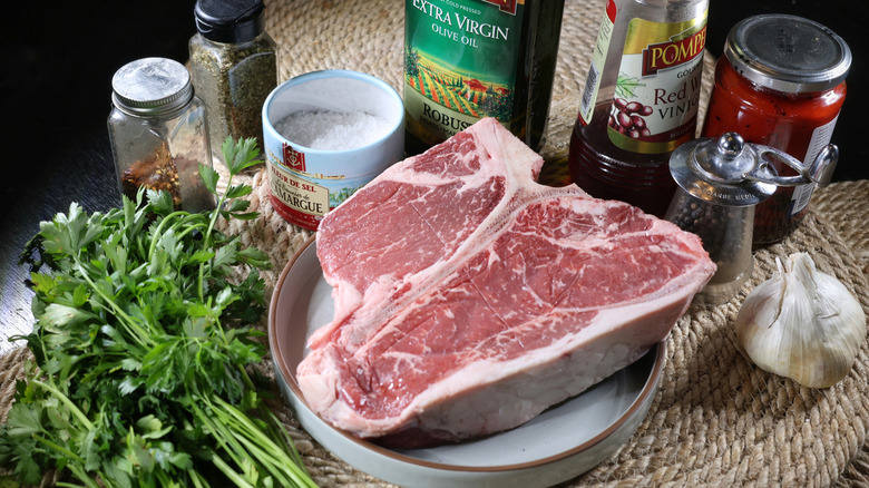 t-bone steak with red chimichurri ingredients laid out on a table