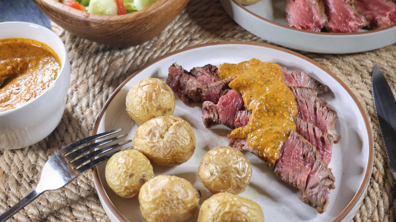 slices of t-bone steak topped with chimichurri rojo sauce on a plate with roasted potatoes
