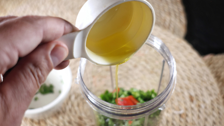 Olive oil pouring from measuring cup into blender