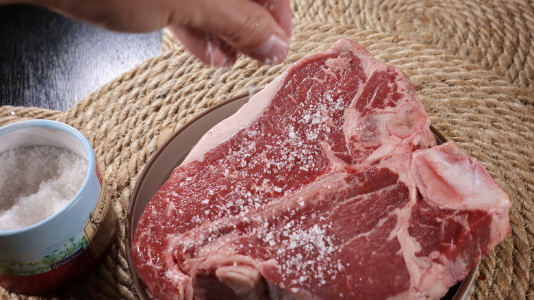 fingers sprinkling coarse salt onto large t-bone steak