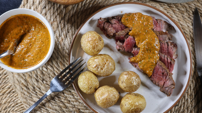 plate of roasted potatoes and thinly-sliced rare steak topped with chimichurri rojo sauce