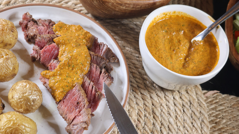 plate of thinly-sliced rare steak topped with chimichurri rojo sauce next to small bowl of the same