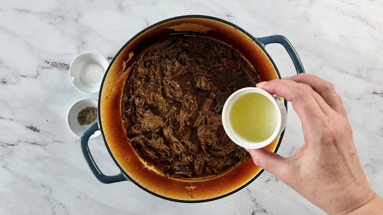 Hand pouring small bowl of lime juice into shredded brisket