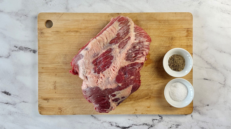 Raw brisket on wooden board with salt and pepper
