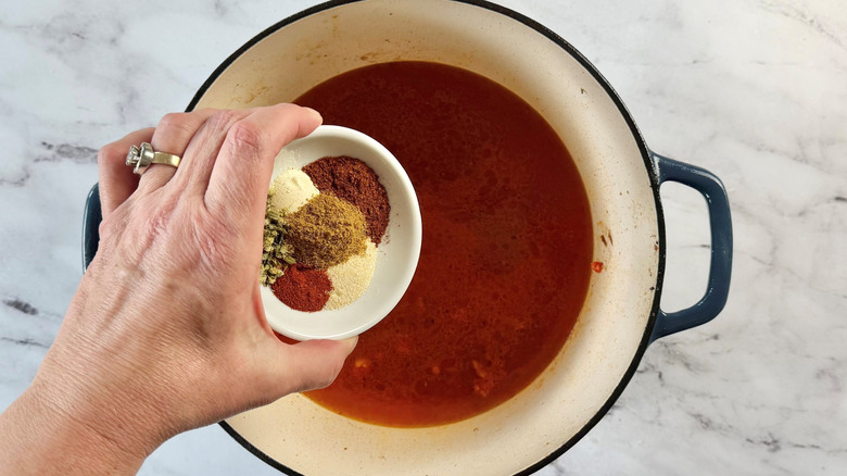 Hand holding bowl of spices over Dutch oven