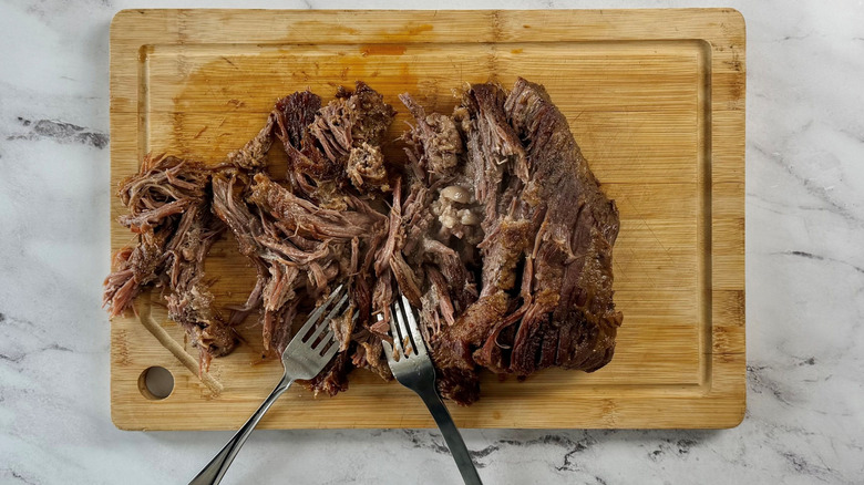 Shredded brisket and forks on wooden board