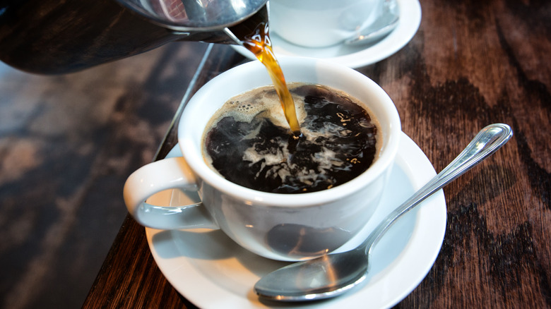 Coffee pouring from pitcher into white cup on saucer.