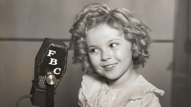 Shirley Temple smiling beside an old-fashioned microphone