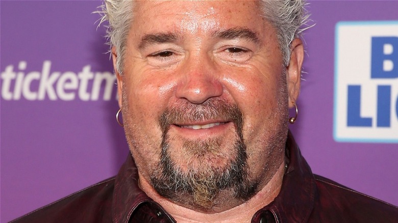 Guy Fieri smiling in front of purple background