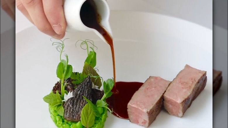 gordon ramsay's suffolk lamb with young peas, girolles, and mint, two pieces of meat and sauce being poured onto plate