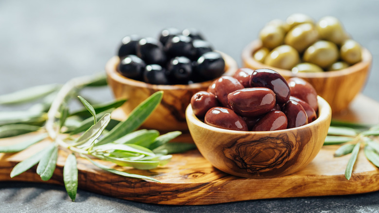 variety of olives in wooden bowls with green leaves