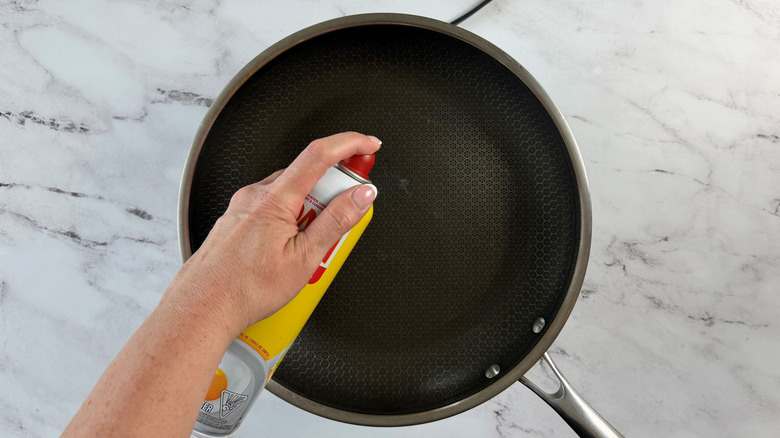Hand spraying cooking spray onto pan