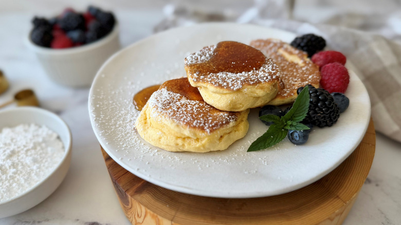 Japanese soufflé pancakes on plate served with powdered sugar, syrup, mint, and berries