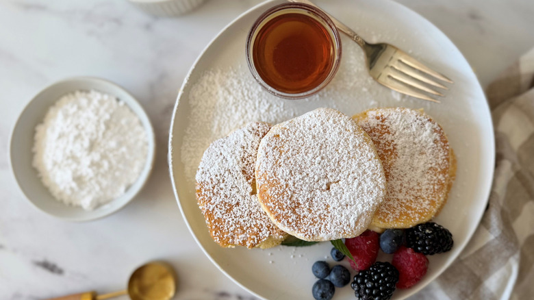 Japanese soufflé pancakes on plate with powdered sugar, syrup, and berries