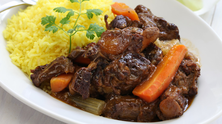 Slow-braised oxtail stew on white plate with rice and carrots