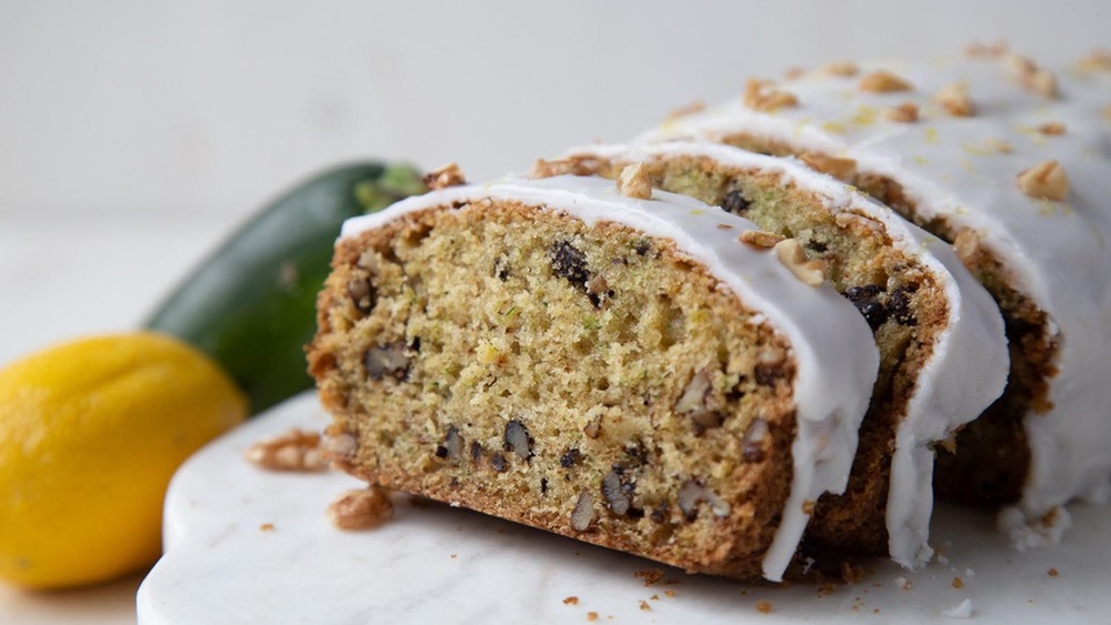 sliced loaf of zucchini walnut bread with lemon glaze on a counter by a lemon and zucchini