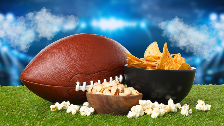 Football on field next to bowls of snacks with stadium background