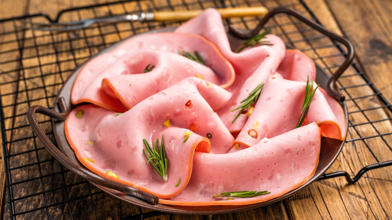A handled plate of carefully folded slices of mortadella meat topped with flecks of rosemary.