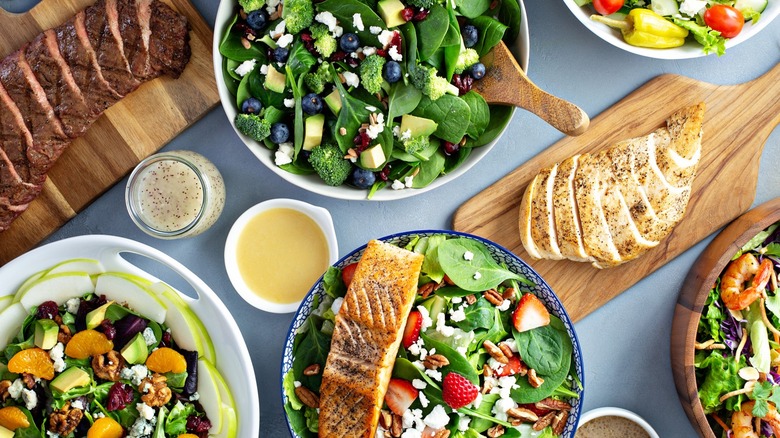 Several bowls of salads with cooked meats on boards. 